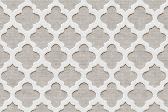 Textured quatrefoil lattice pattern on beige fabric surface with raised white overlay creating repeating geometric ornament and subtle shadowing for textile or wallpaper design