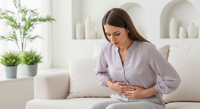 Woman holding her stomach in pain on a sofa, symbolizing discomfort, illness, or digestive issues, relevant for medical concepts.