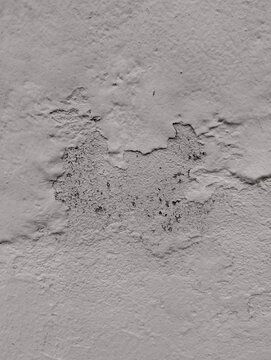 Close up of a grey wall with large patch of peeling paint and visible rough concrete surface