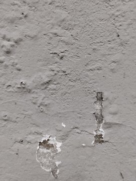 Detailed view of crumbling grey paint on a rough wall surface with visible cracks and decay signs