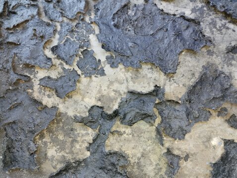 Macro view of dark peeling paint on a concrete wall creating a rough and distressed texture look.