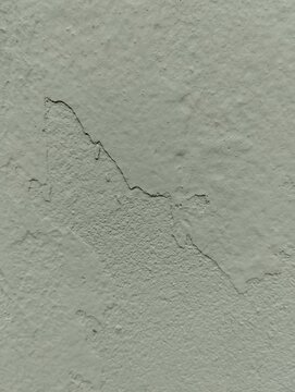 Macro view of light green painted wall showing peeling paint and structural surface cracks