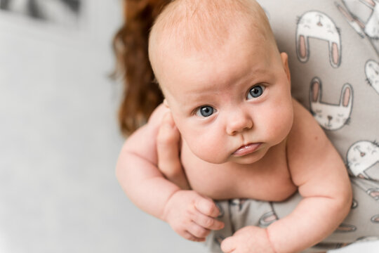 Mother holds baby 5-6 months old in her arms at home while the child looks at camera, everyday care and motherhood