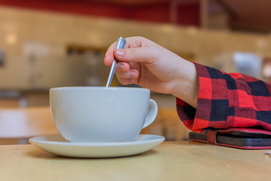 Hand stirring coffee in white cup at restaurant table
