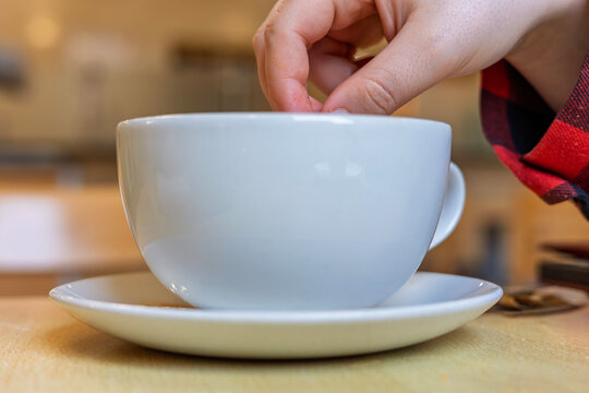 Hand stirring coffee in white ceramic cup on saucer