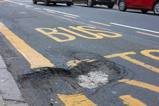 Large pothole in bus lane road surface with yellow markings