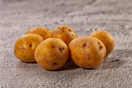 Fresh unpeeled potatoes with earthy skin on textured gray surface, natural lighting, shallow depth of field, rustic food photography