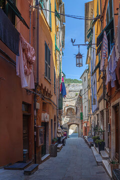 Portovenere, Italy - May 25, 2026: A narrow, picturesque street (*caruggio*) lined with buildings in warm tones, featuring laundry hung out to dry and a suspended lantern.