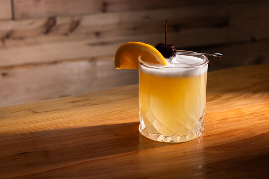 Beautiful Whiskey sour served on the rocks garnished with an orange slice and a dark cherry