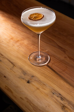 Beautiful Whiskey sour served up in a couple glass garnished with a dehydrated orange wheel with a warm wooden surface and background texture.