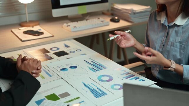 Two businesswomen discussing and analyzing financial data from charts and graphs during a meeting in the office, focusing on corporate strategy, performance, and investment planning