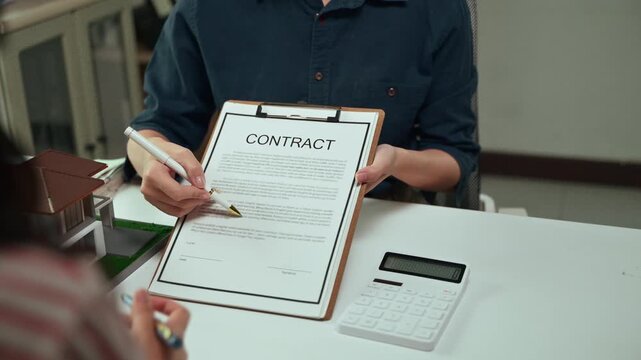 Close up view of a real estate agent's hands pointing with a pen to the signature line on a house purchase contract, explaining the terms and conditions to a client before signing the document