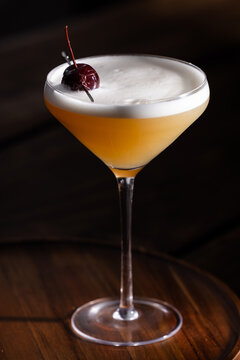 Beautiful Whiskey sour served up in a couple glass garnished with a dehydrated orange wheel with a warm wooden surface and background texture.