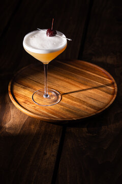 Beautiful Whiskey sour served up in a couple glass garnished with a dehydrated orange wheel with a warm wooden surface and background texture.