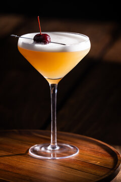 Beautiful Whiskey sour served up in a couple glass garnished with a dehydrated orange wheel with a warm wooden surface and background texture.