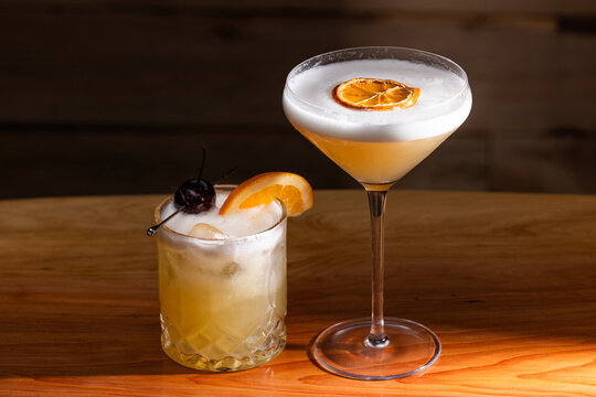 Beautiful Whiskey Sour served two ways, up and on the rocks with a warm wooden surface and background texture.