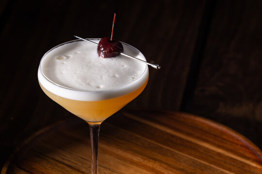 Beautiful Whiskey sour served up in a couple glass garnished with a dehydrated orange wheel with a warm wooden surface and background texture.