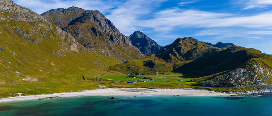 Aerial drone view of a white sand beach with turquoise water and green mountains under a blue sky in northern Norway © Quality by Simon