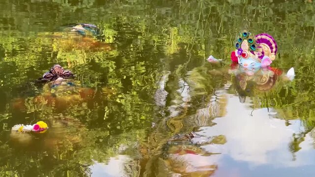 Static shot of colorful Lord Ganesha idols floating in river water after Ganesh Chaturthi with scenic palm tree reflections in Goa, India