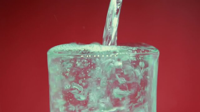 Glass of Water in isolated close Up  spilling overflowing the rim on red background. A conceptual abstract representation of breaking points, overcoming limits.4k 60fps 