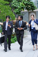 Fototapeta premium A multiethnic business team of three colleagues commute on foot while handling calls and messages beside the polished facade of a new mixed use city (frame 173)