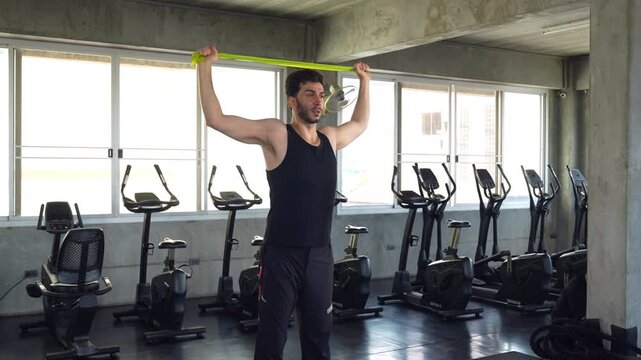 Man stretching with resistance band overhead during shoulder mobility workout in modern gym, focusing on flexibility, strength training, and functional fitness exercise.