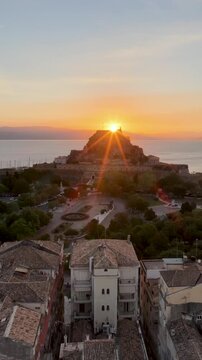 Vertical Aerial View of Old Fortress Castle and Sunstar at Sunrise over Historic Old Town Rooftops in Corfu Island Greece 4K
