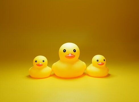 Three yellow rubber ducks on a monochrome background. The central one is large, the sides are small. Studio subject shooting.