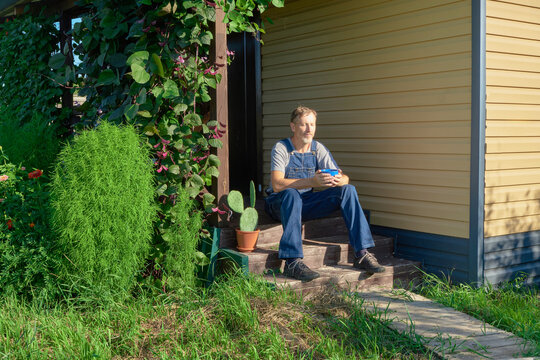 Man in overalls relaxing on porch steps with cup outdoors