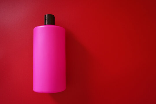Pink plastic bottle with a black lid on a red background. Subject shooting, long shadow, place under the label.
