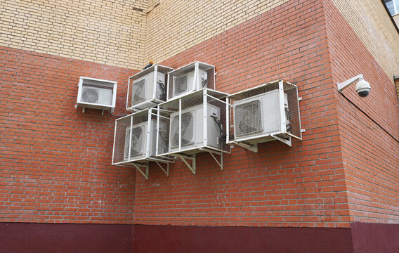 A brick wall with separate outdoor units of air conditioners in protective grilles. Mounting on brackets, cable wiring, rotary surveillance camera