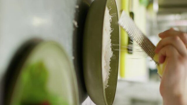 Vertical video. Shredding cheese. Food preparation. Unrecognizable professional chef man hands making presentation cooking parmesan salad dish on plate in restaurant.