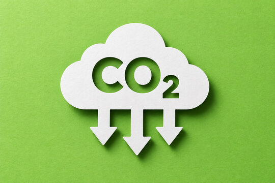 White paper cloud cut out shape displaying carbon dioxide emission symbol with pointing arrows downward against a textured bright lime green background paper surface showing minimalist conceptual eco 