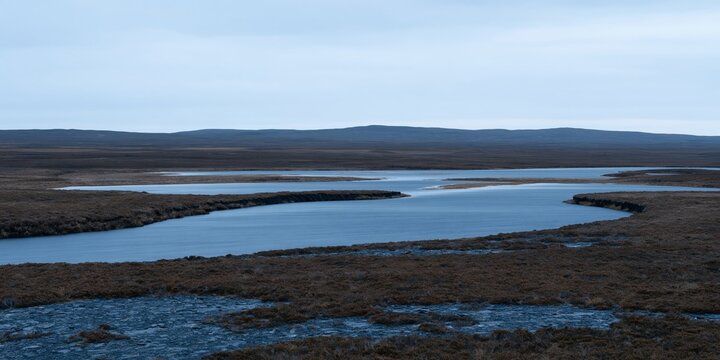 Landscape of a peat moor with still pools and a distant ridge under a flat grey sky, featuring wet rock for travel and outdoor campaigns