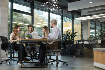 Obraz premium A view through a glass partition shows a modern, busy office interior. Business people are working at desk
