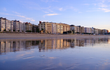 Obraz premium Sunset over Zurriola beach with city reflection on wet sand, San Sebastian, Basque Country, Spain