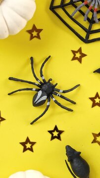Top view of plastic spider and black bats spinning on yellow background in vertical orientation, Halloween holiday decoration rotating. Spooky seamless background. Halloween backdrop