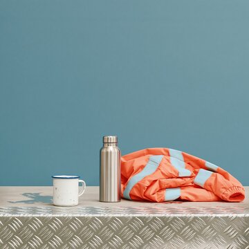 Steel flask and folded reflective jacket on a metal step with an enamel cup, glowing under night lights for emergency services and copy space