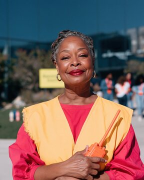 Black woman fire warden in a yellow hi-vis tabard holding an orange radio, calm and capable during a workplace safety fire drill for EHS software
