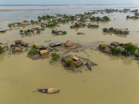 Rajshahi District, Bangladesh - 19 September 2026: Aerial view of flooded rural landscape with small huts on isolated land patches and people in traditional wooden boats.