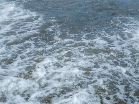 Rough ocean waves crashing against the rocky shore creating white foam with blue water texture and natural light captured from a high angle looking straight down