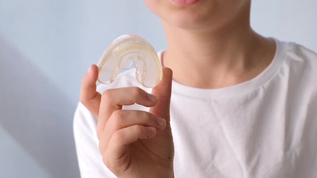 The child holds a clear dental aligner in their fingers. Orthodontic treatment, dental care, oral hygiene. High quality 4k footage.