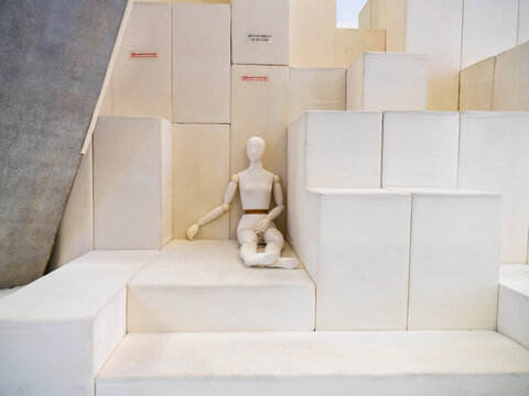 View of a wooden mannequin sitting on white geometric blocks in a minimalist interior space in Seoul, Seoul, South Korea.