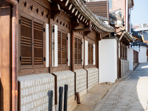 View of traditional hanok architecture with wooden lattice windows and stone walls along a quiet alley in Bukchon Hanok Village, Seoul, South Korea.