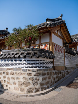 View of the traditional hanok architecture with stone walls, tiled roofs, and a pine tree at Bukchon Hanok Village in Seoul, Seoul, South Korea.