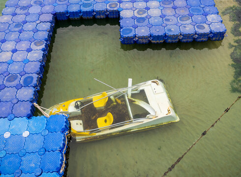 View of a partially submerged pedal boat with yellow seats moored to a blue modular floating platform in the clear water of Busan, Busan, South Korea.
