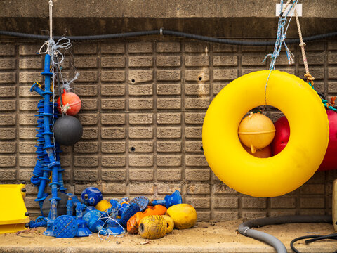 View of colorful fishing buoys, floats, and a yellow life ring hanging against a textured concrete wall in Busan, Busan, South Korea.