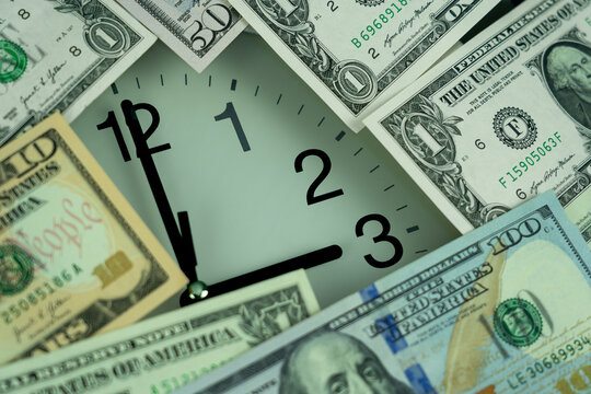 Close-up conceptual view of analog clock surrounded by different US Dollars (USD), symbolizing the financial cost, time loss, and economic impact of changing the clocks for Daylight Saving Time