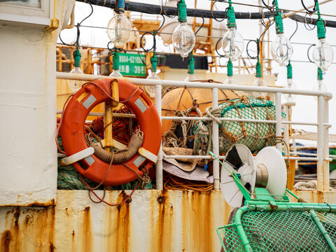 View of a fishing boat deck featuring a bright orange lifebuoy, tangled fishing nets, and rows of light bulbs for night fishing in Busan, Busan, South Korea.