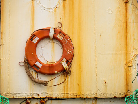 View of an orange lifebuoy mounted on a weathered and rusted metal ship hull in Busan, Busan, South Korea.
